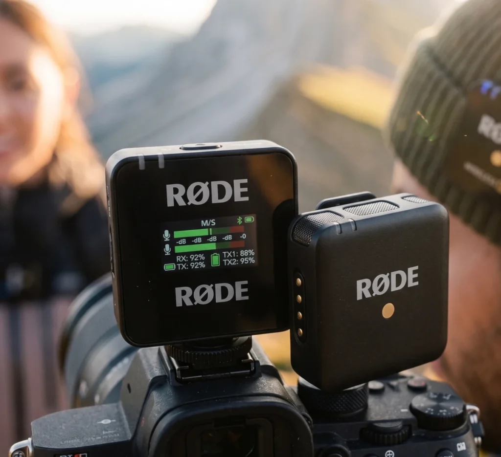 RØDE Wireless PRO receiver mounted on a camera hot shoe showing active audio levels and battery status, next to a wireless transmitter clip in an outdoor setting.